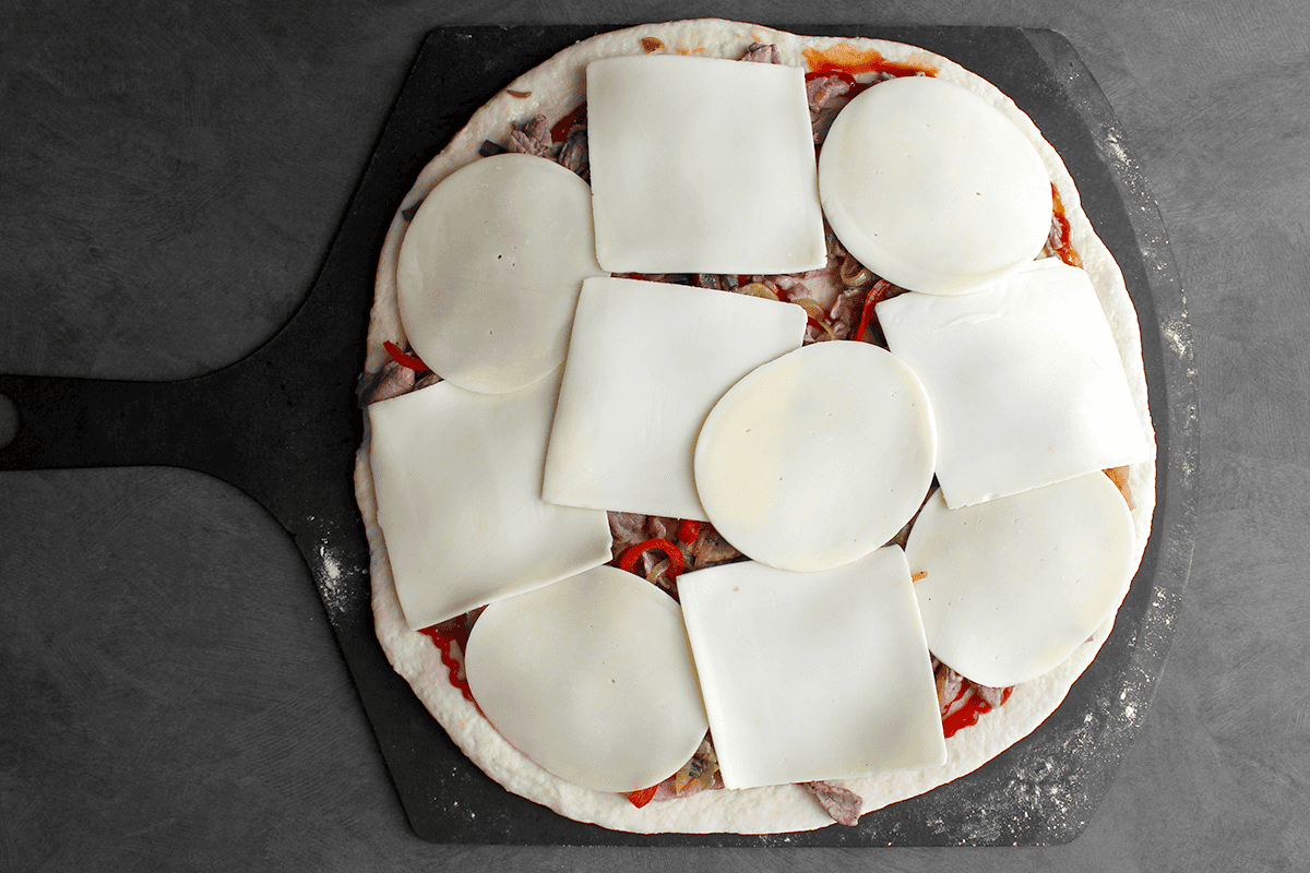 Cheese steak pizza with provolone and American cheeses, before baking