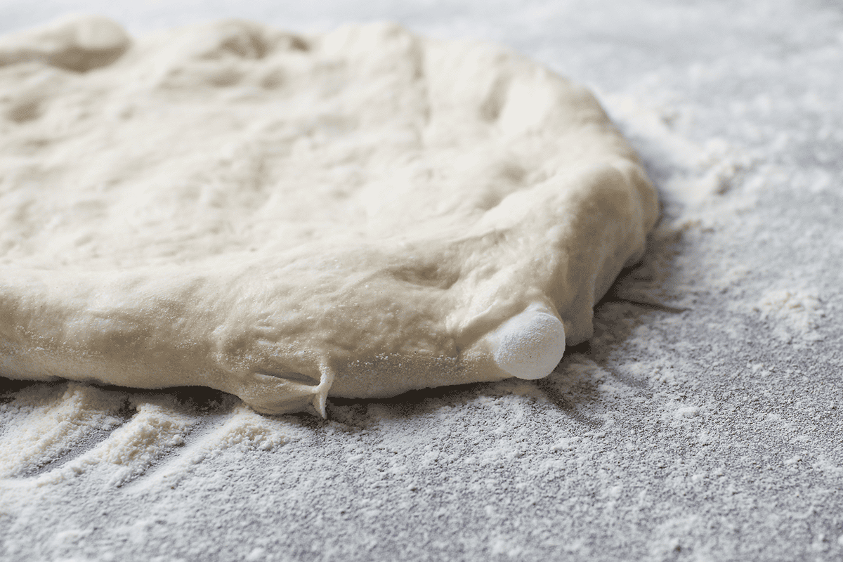 partially stretched ball of pizza dough on counter with bubble