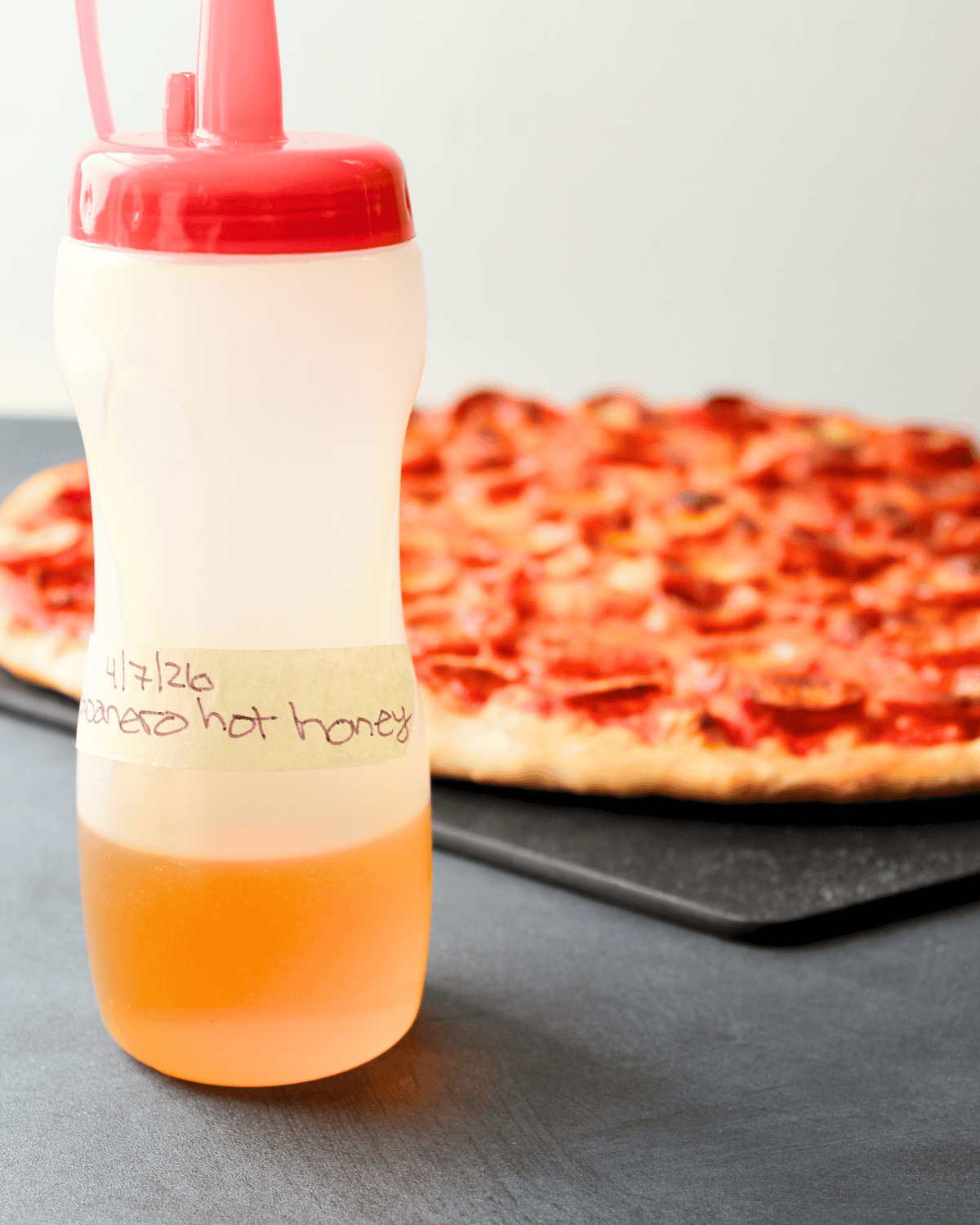 How to make hot honey: Finished honey in squeeze bottle with pizza in background