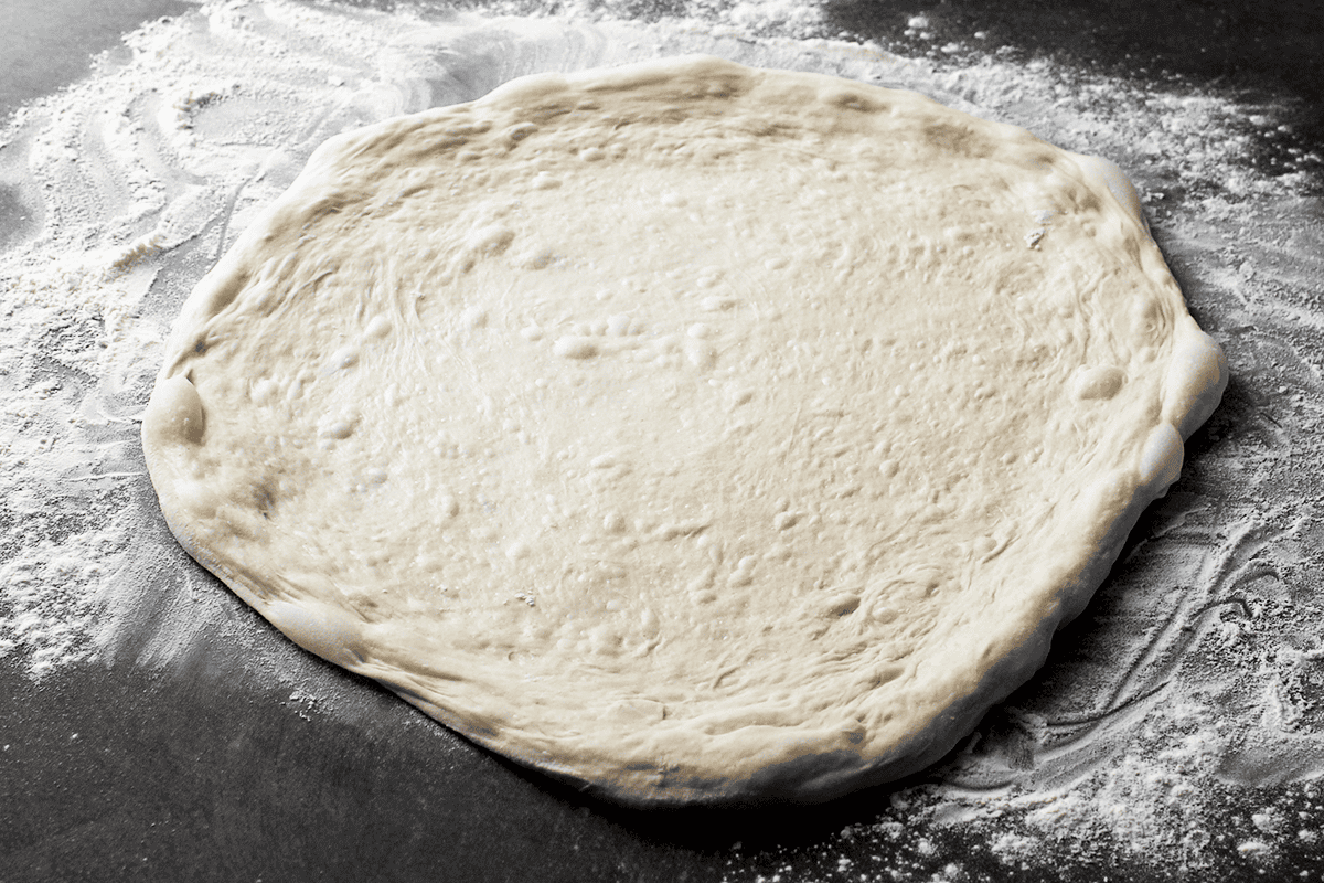 stretched-out pizza dough on counter dusted with 00 flour